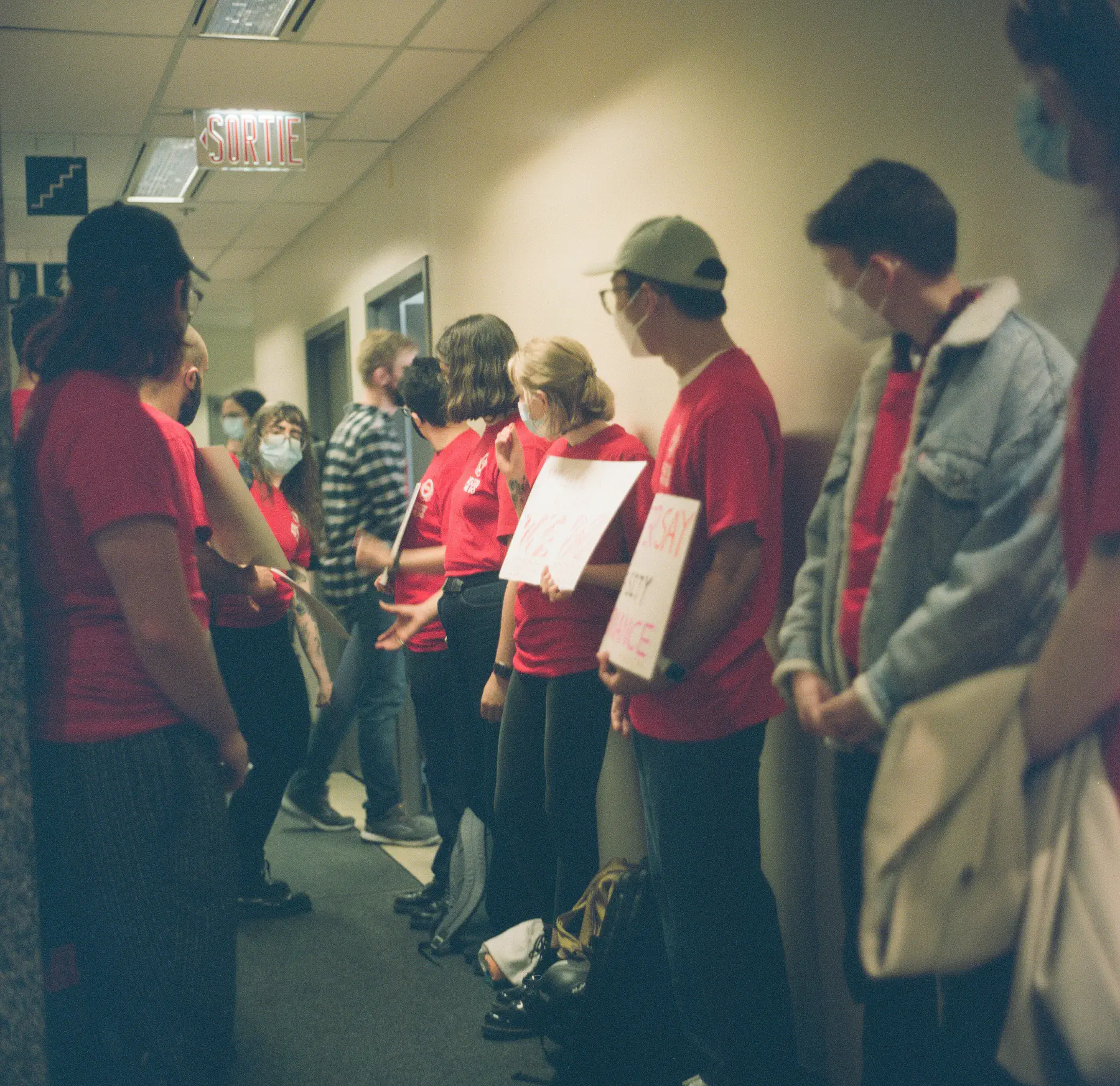 Photo of AGSEM members lining the hall with signs expressing support of a fair contract as McGill representatives and the Bargaining Committee enter the negotiation room. Photo: Riley Hannah Lewicki, @analog_girl_photos (September 21, 2023).