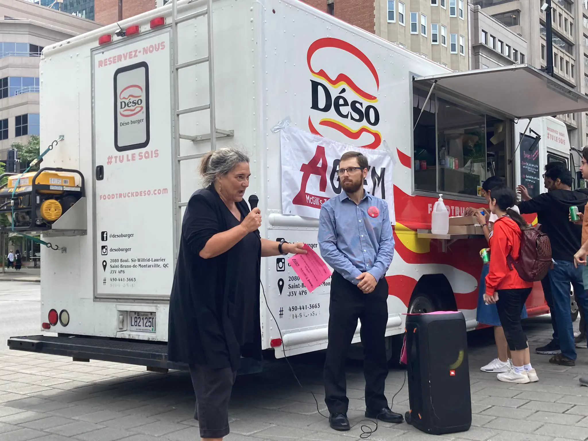 Photo of Dominique Daigneault, President of the Conseil central du Montréal métropolitain (CCMM-CSN), giving a speech at rally in support of invigilator negotiations, AGSEM President Mario Roy pictured behind (September 1, 2022).